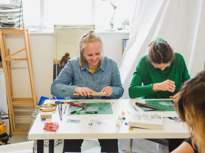 A mum and daughter work side by side in a craft workshop.